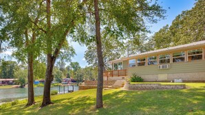 A lakeside house with a deck, a stone retaining wall, and a grassy lawn. - Kilgore Lakefront Home w/ Private Dock & Pier! (Kilgore)