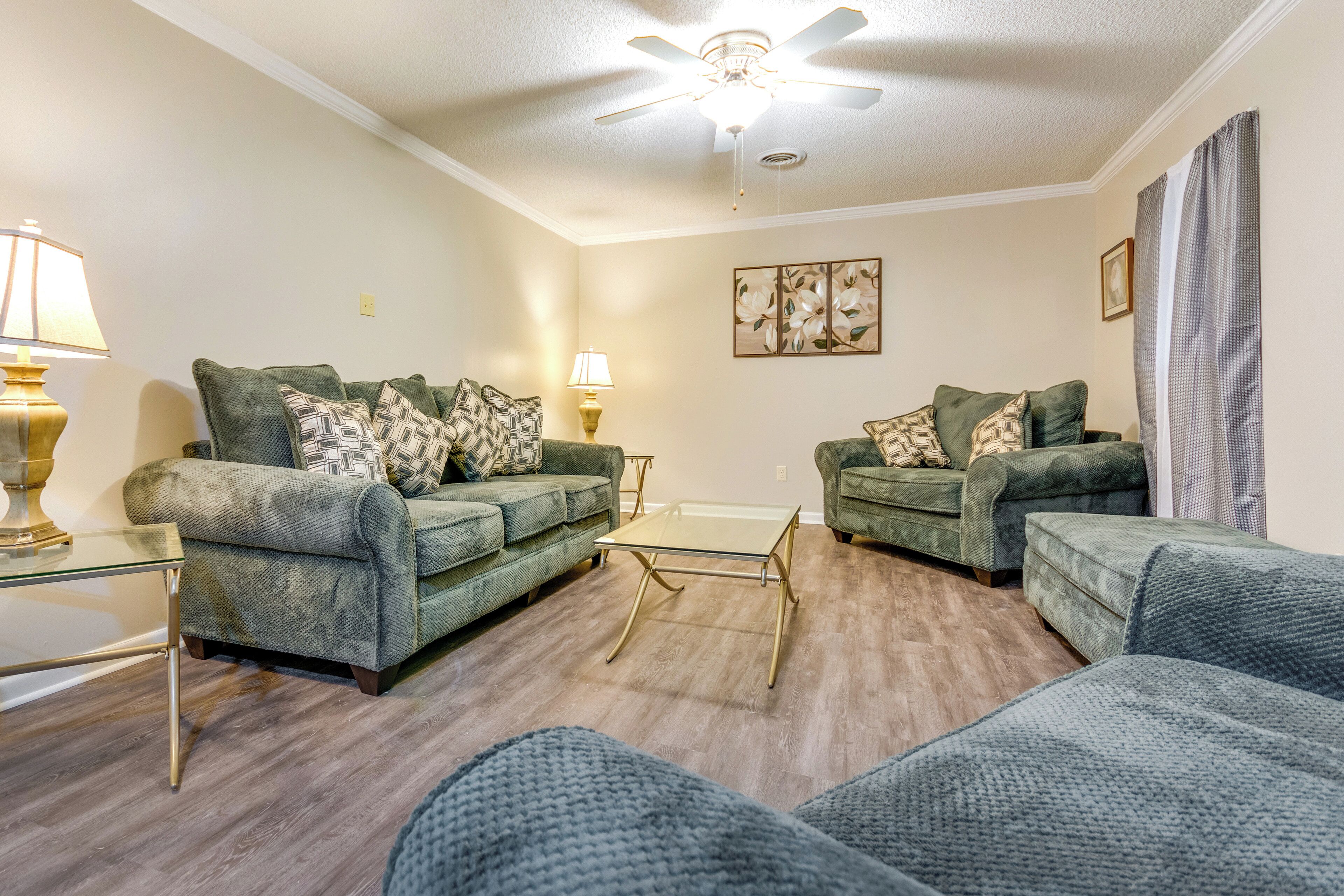 A living room with two green sofas, a glass coffee table, and a ceiling fan.