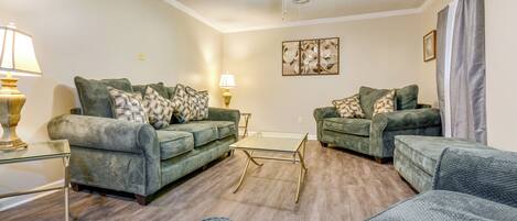 A living room with two green sofas, a glass coffee table, and a ceiling fan.
