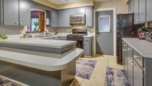 Una cocina moderna con armarios grises, una isla central, electrodomésticos de acero inoxidable y un ventanal amplio.