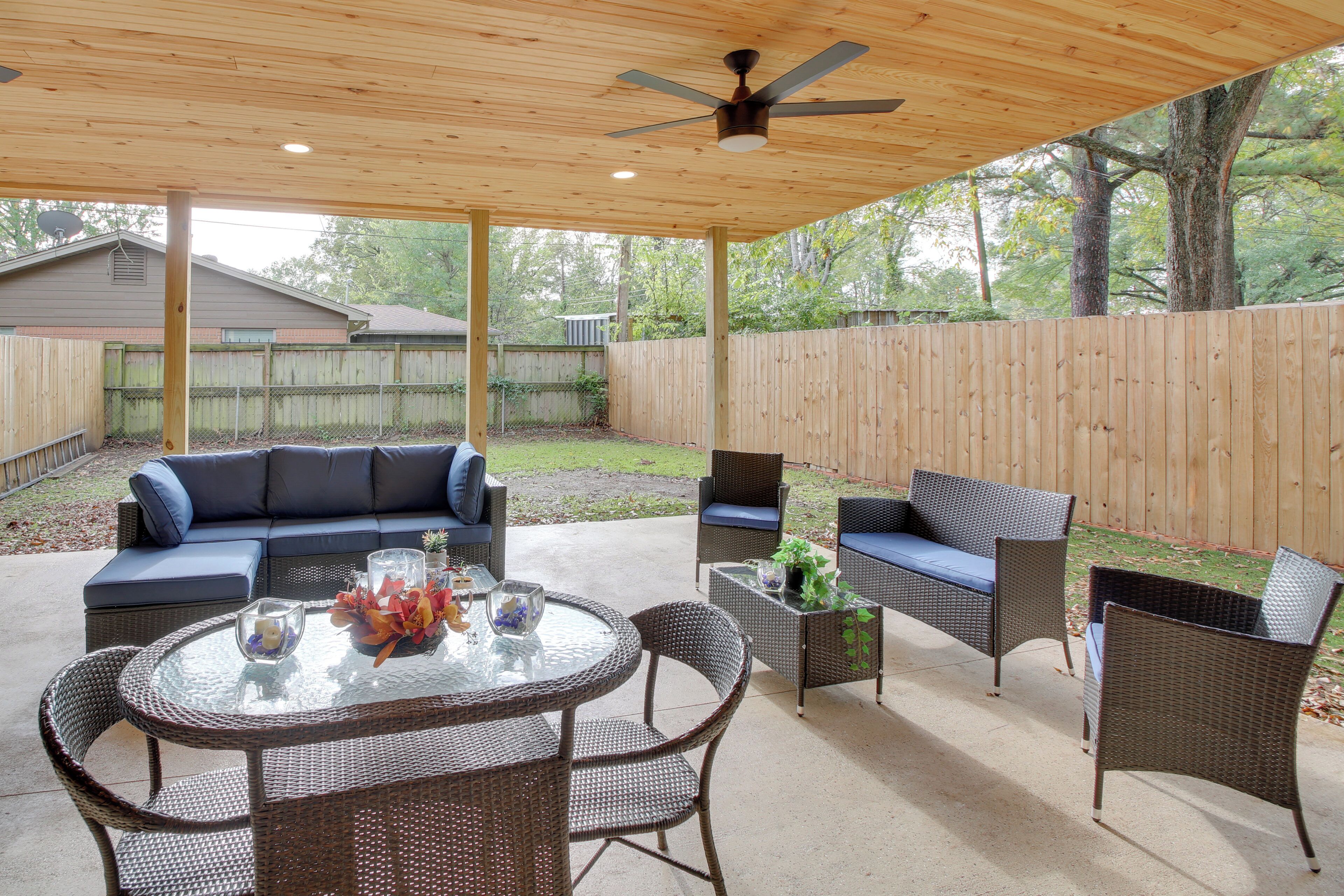 An outdoor patio with a round table, wicker chairs, a sofa, and a ceiling fan.