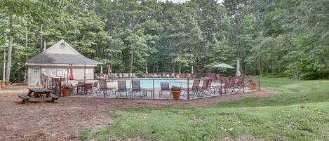 A pool area with lounge chairs and a small pavilion, surrounded by trees.