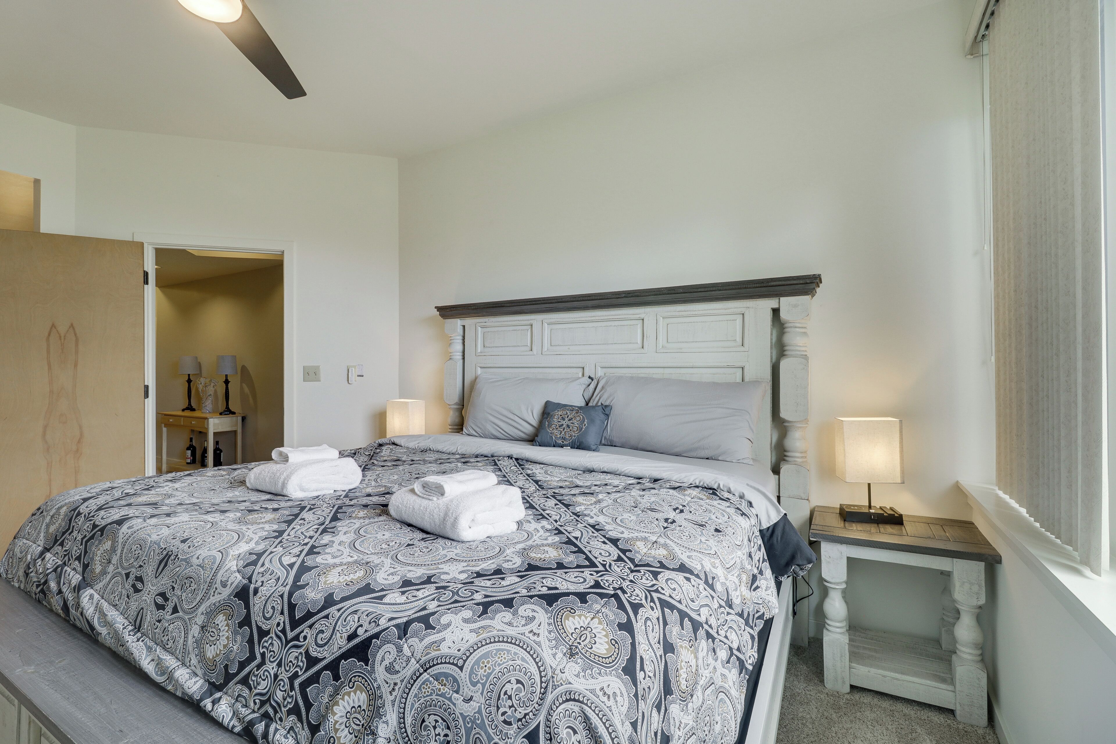 A neatly made bed with a patterned bedspread, a bedside table with a lamp, and a door leading to another room.