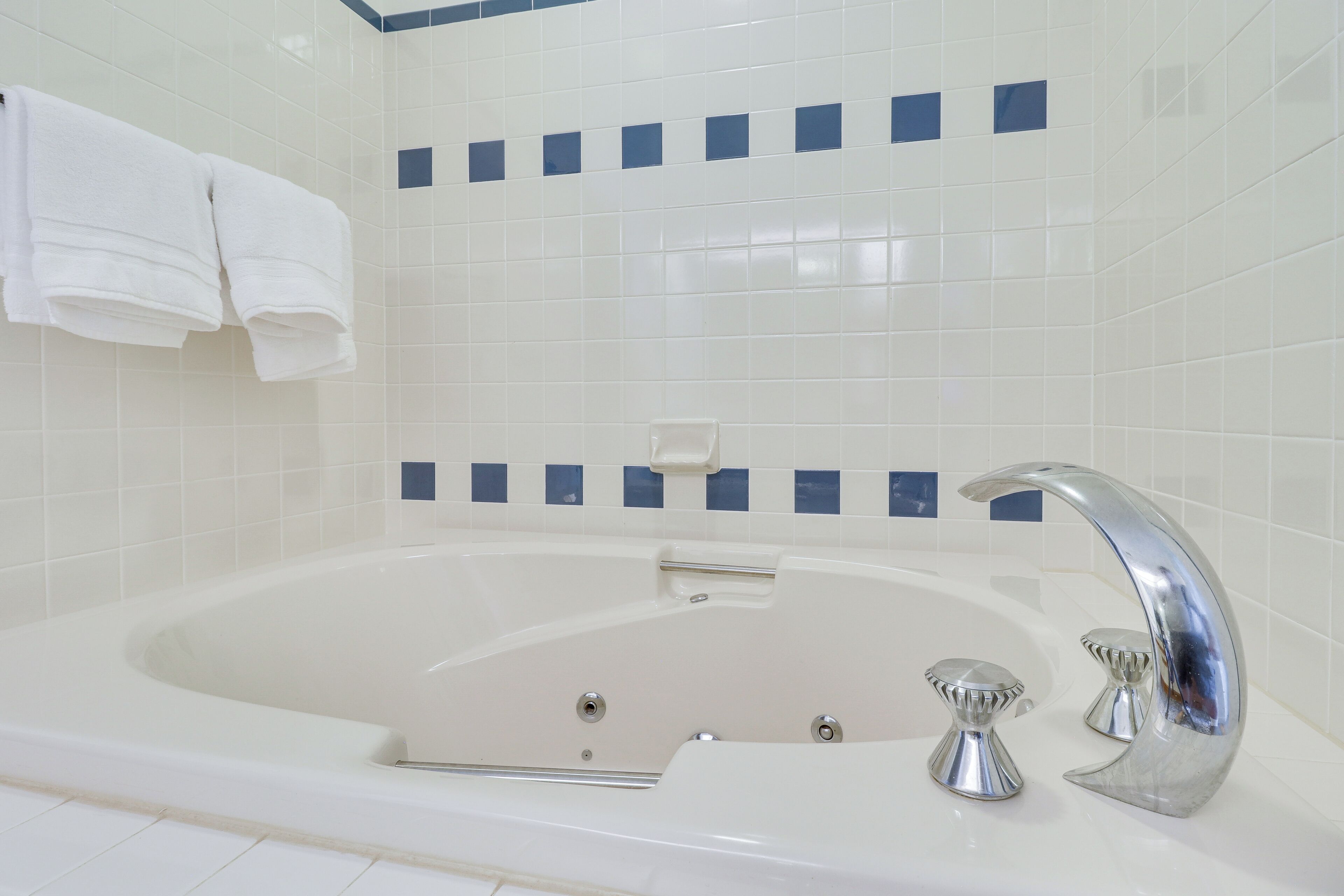 Un bagno moderno con una vasca da bagno ampia, piastrelle bianche e una parete rivestita in piastrelle blu.