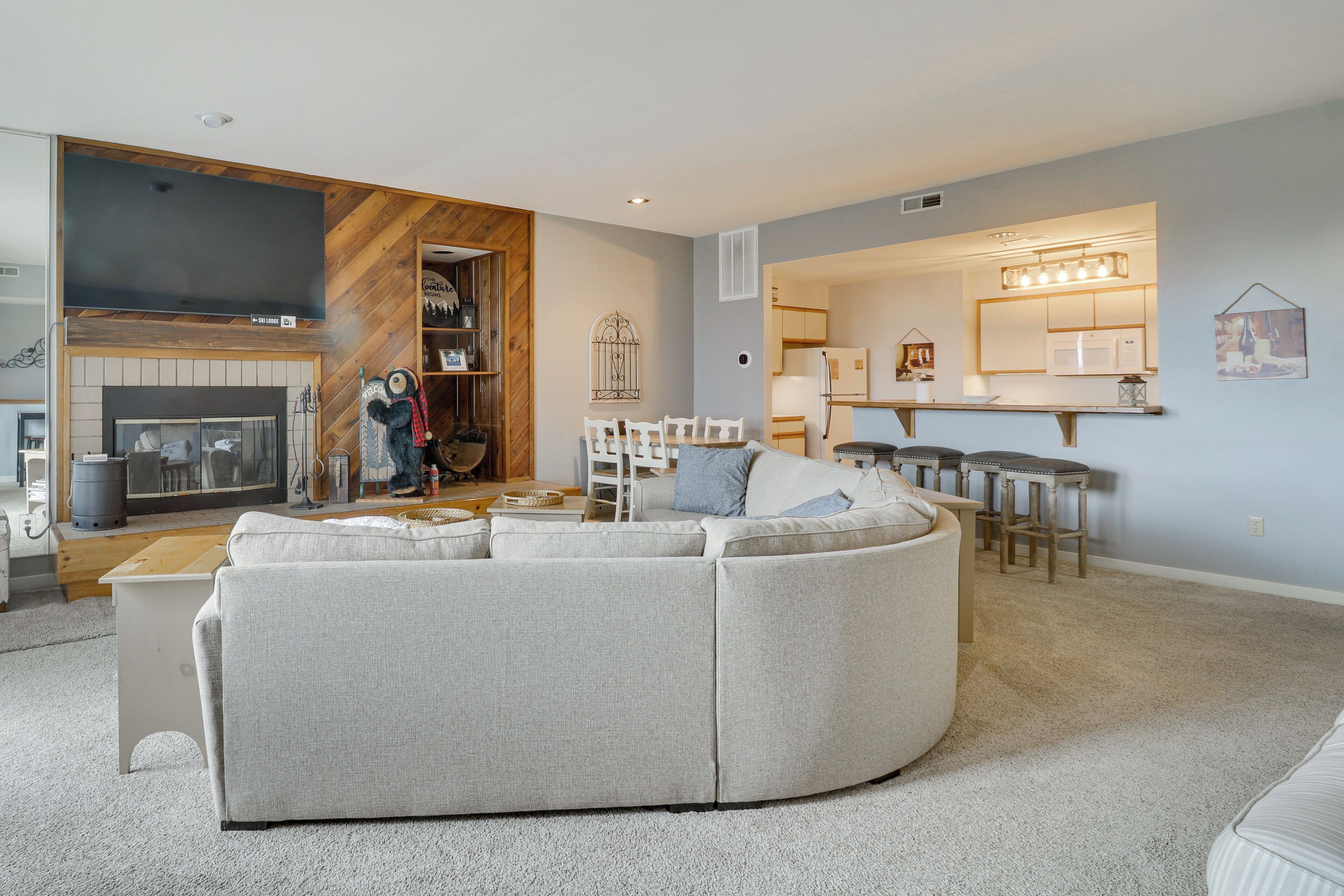 A modern living room with a sectional sofa, a fireplace, and a kitchen area with bar stools.