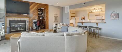 A modern living room with a sectional sofa, a fireplace, and a kitchen area with bar stools.