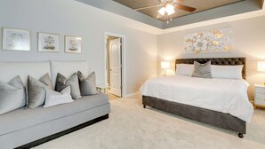 Une chambre à coucher comprenant un lit, un canapé, un ventilateur de plafond, des œuvres d’art encadrées et une porte.