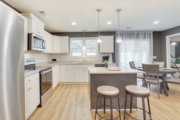 Una cocina moderna con armarios blancos, electrodomésticos de acero inoxidable y una isla central con taburetes de bar.