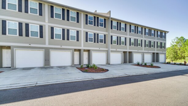 A multi-story residential building with a row of garage doors, a concrete driveway, and small landscaped areas with plants. - Spacious D'iberville Townhome Near Beach & Casino! (D'Iberville)