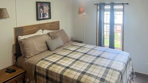 A bedroom with a bed, nightstand, lamp, and window with curtains. - Creekfront Max Meadows Mobile Home With Deck! (Max Meadows)