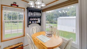 A dining area with a wooden table, white chairs, a chandelier, and a view of a backyard. - Creekfront Max Meadows Mobile Home With Deck! (Max Meadows)