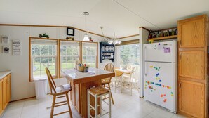 A kitchen with a wooden table, chairs, a refrigerator, and a window with a view of greenery. - Creekfront Max Meadows Mobile Home With Deck! (Max Meadows)