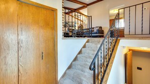 Un escalier avec une porte en bois sur la gauche, un coin salon avec des sièges rembourrés sur la droite et un ventilateur de plafond au-dessus.