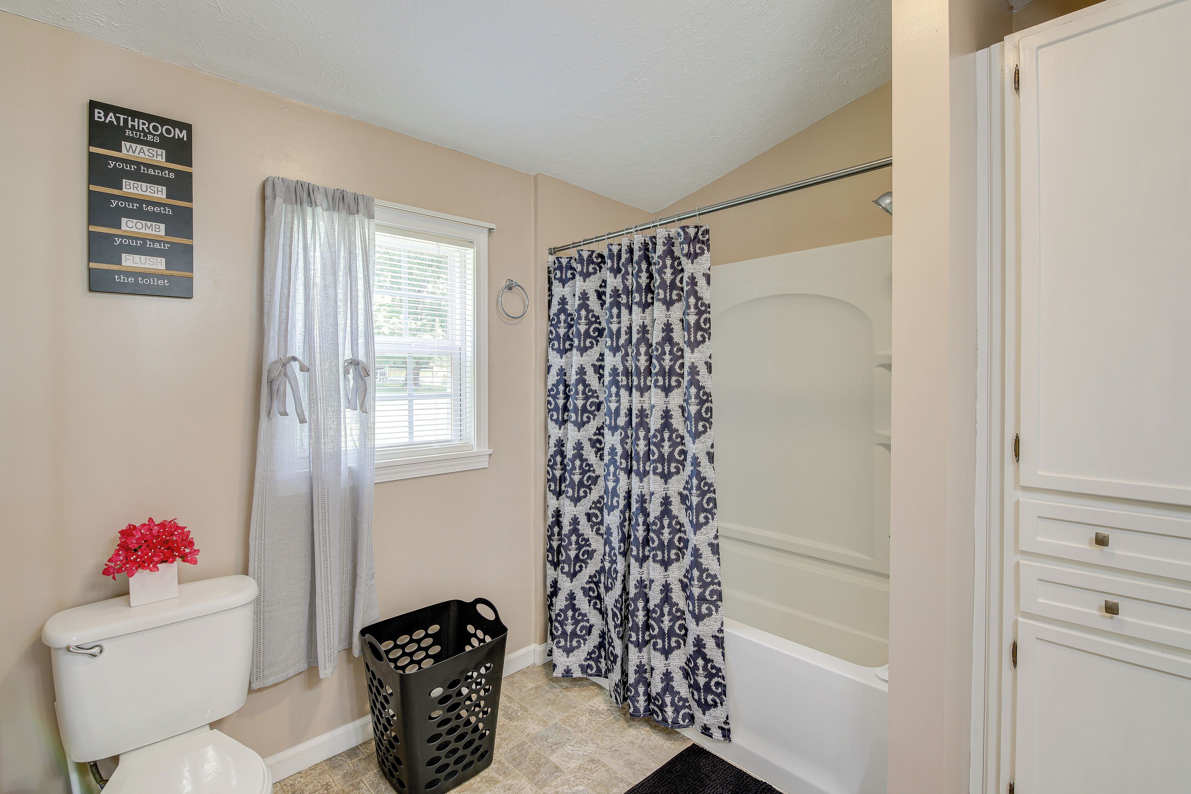 A bathroom with a toilet, a shower curtain, a basket, and a sign listing bathroom rules.