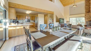 Un vaste espace dédié à la salle à manger, avec une longue table en bois, de nombreuses chaises et un plafond haut avec des poutres apparentes.