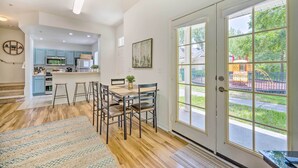 Una cocina moderna con una isla central, un comedor con mesa y sillas, y un amplio ventanal corredero que da a un patio.