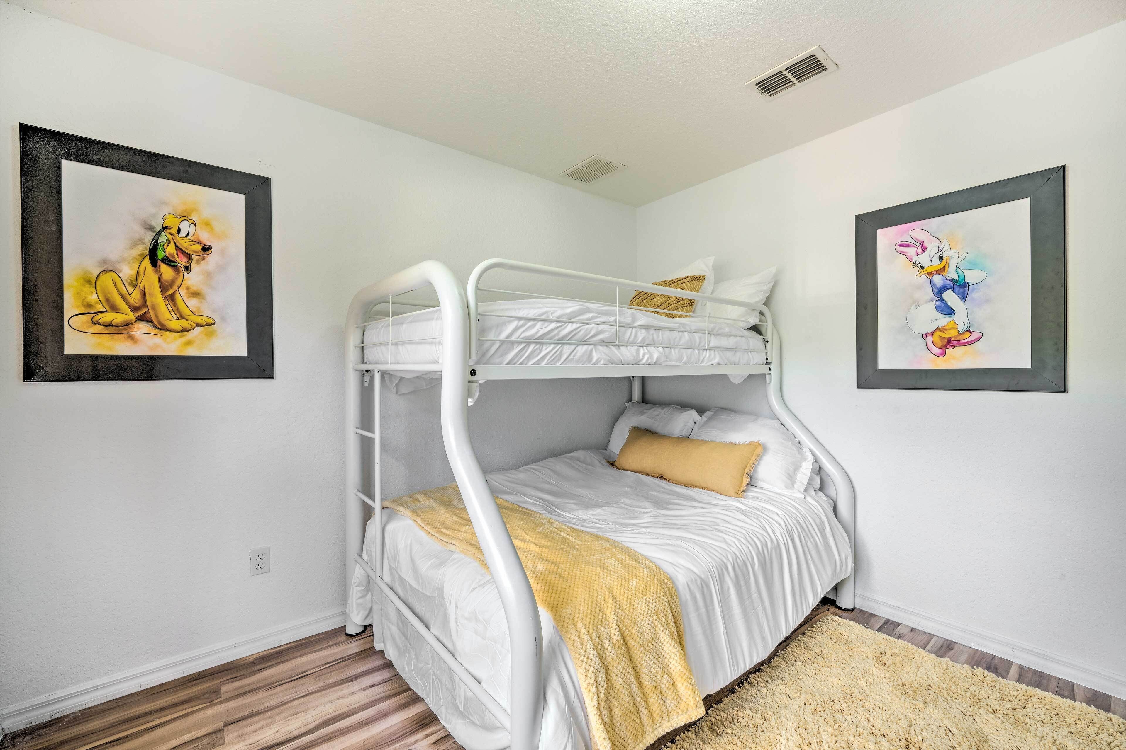 A bunk bed room with a yellow blanket, white walls, and two framed pictures.
