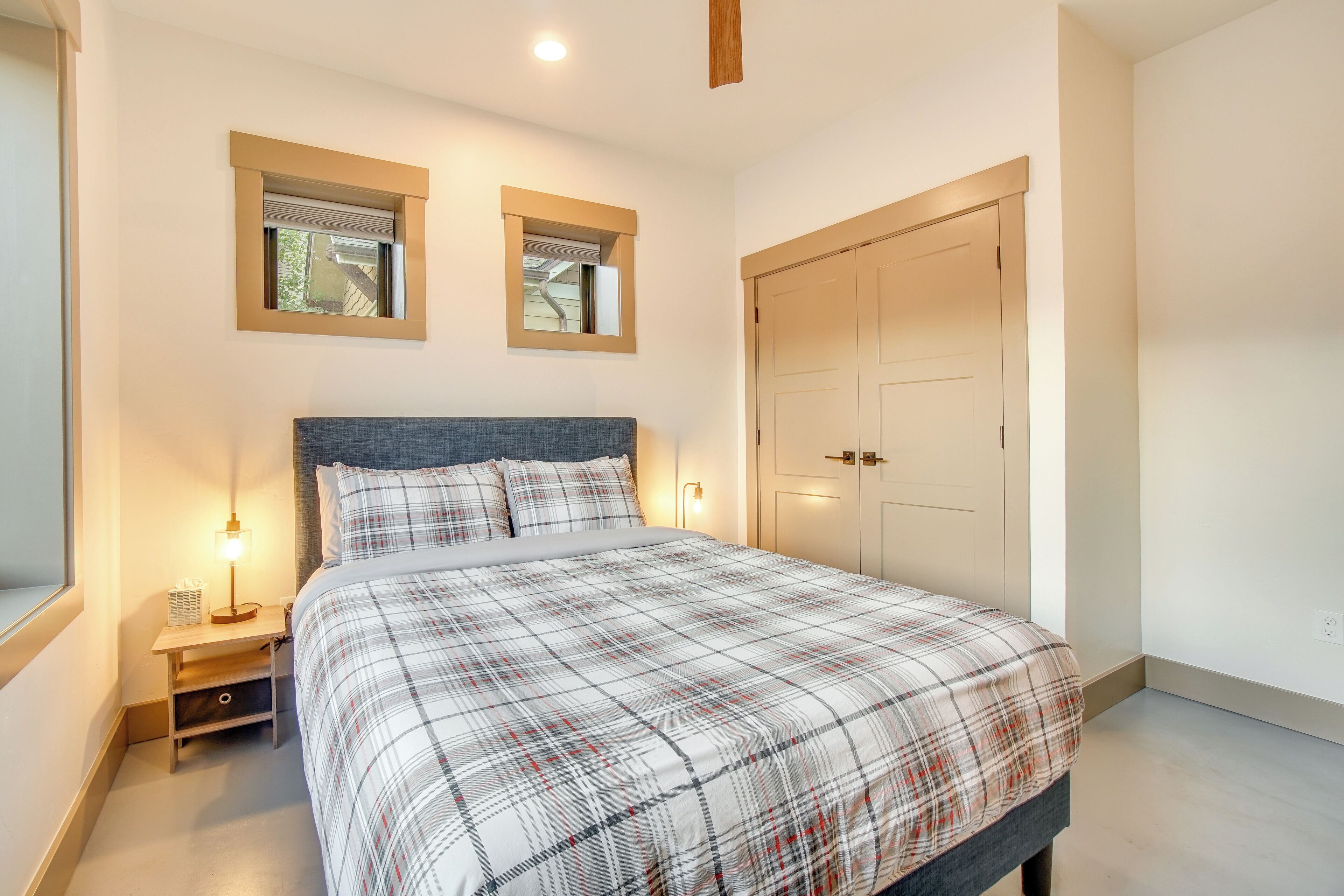 A bedroom with a bed, bedside tables, a wardrobe, and two windows.