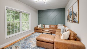 A modern living room with a sectional sofa, a coffee table, and a large window with a view of greenery. - Asheville Retreat ~ 6 Mi to Biltmore & Downtown! (Asheville)