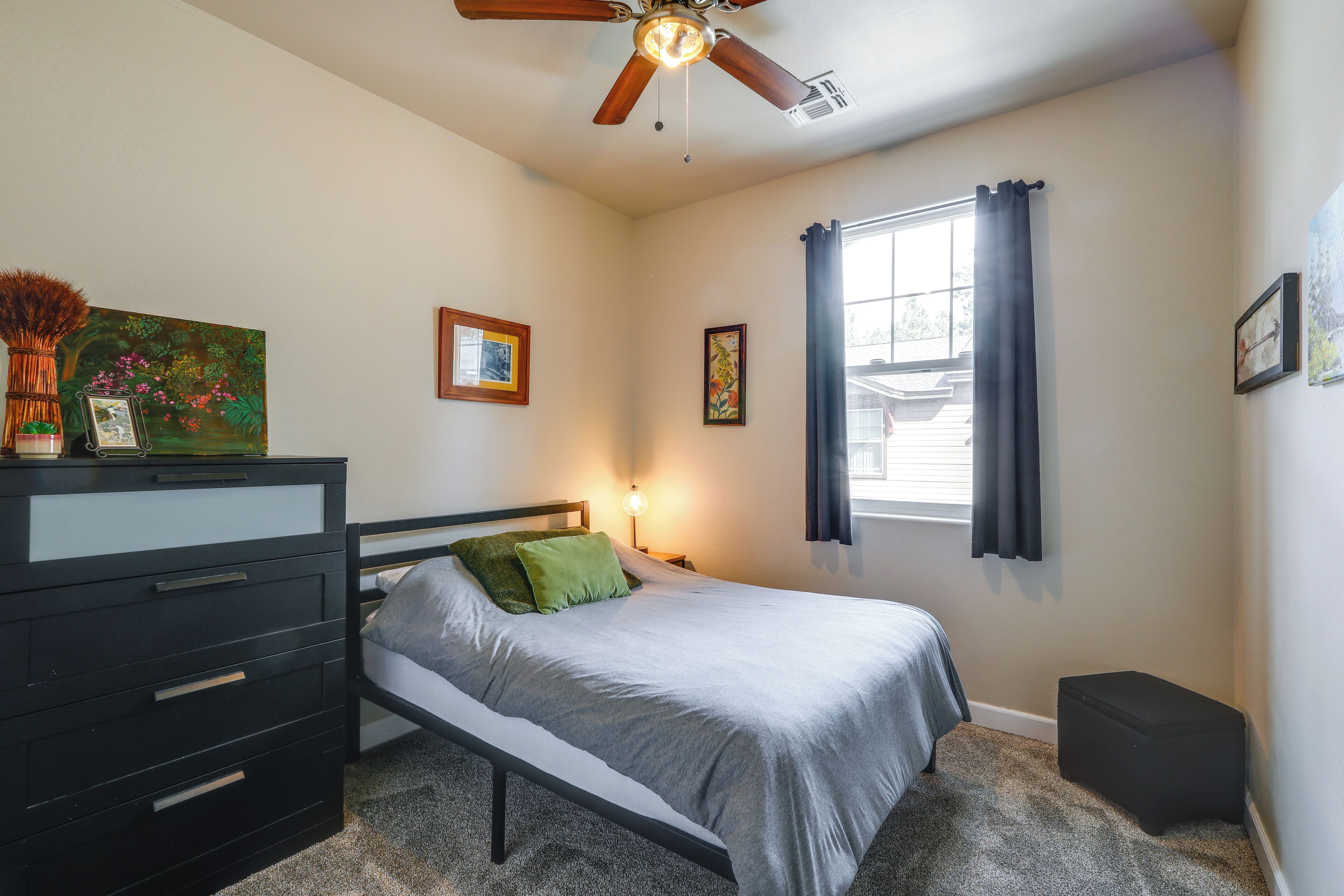 Une chambre à coucher avec un lit, une commode, une table de chevet et une fenêtre avec des rideaux.