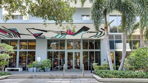 A modern building with large glass windows, a covered entrance area with potted plants, and a clear view of the interior through the glass. - High-end Miami Condo w/ City & Bay Views!!! (Miami)