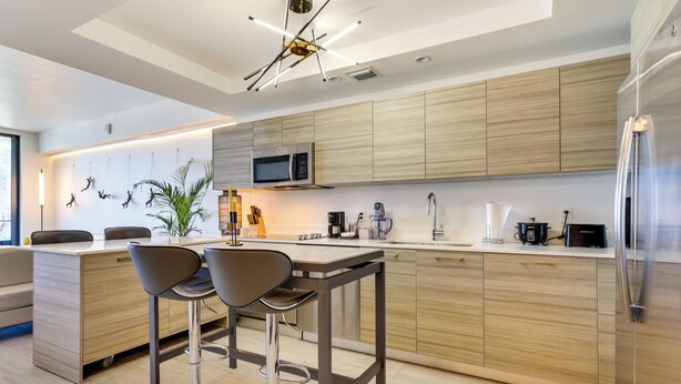 A modern kitchen with wooden cabinets, a stainless steel refrigerator, a microwave, and two bar stools. - High-end Miami Condo w/ City & Bay Views!!! (Miami)