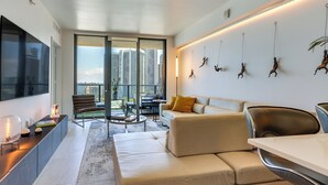 A modern living room with a sofa, a coffee table, and a TV. There is a balcony with a view of buildings. - High-end Miami Condo w/ City & Bay Views!!! (Miami)