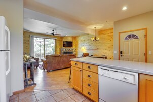 A kitchen with wooden cabinets, a dishwasher, a dining area with a table and chairs, and a TV mounted above the fireplace.
