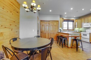 A kitchen with wooden cabinets, a central island with stools, a dining table with chairs, and a chandelier.