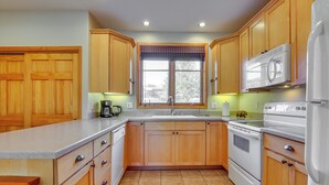 A kitchen with wooden cabinets, a large window with blinds, a sink, a stove, and a refrigerator. - Walk to Main Street: Grand Lake Condo w/ Patio (Grand Lake)