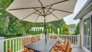 A wooden deck with a table and chairs under a large umbrella, surrounded by white railings and greenery. - Rye Coastal Retreat w/ Deck & Outdoor Dining (Rye)