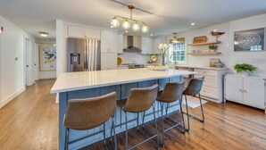 A modern kitchen with a central island, bar stools, white cabinetry, and a stainless steel refrigerator. - Rye Coastal Retreat w/ Deck & Outdoor Dining (Rye)