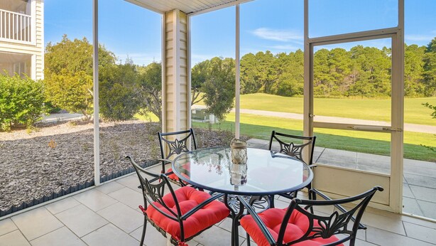 A covered patio with a glass table and chairs, overlooking a well-maintained lawn and trees. - Myrtle Beach Condo w/ Community Perks (Myrtle Beach)