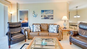 A living room with a brown leather sofa, a glass coffee table, and a painting of a lighthouse. - Myrtle Beach Condo w/ Community Perks (Myrtle Beach)