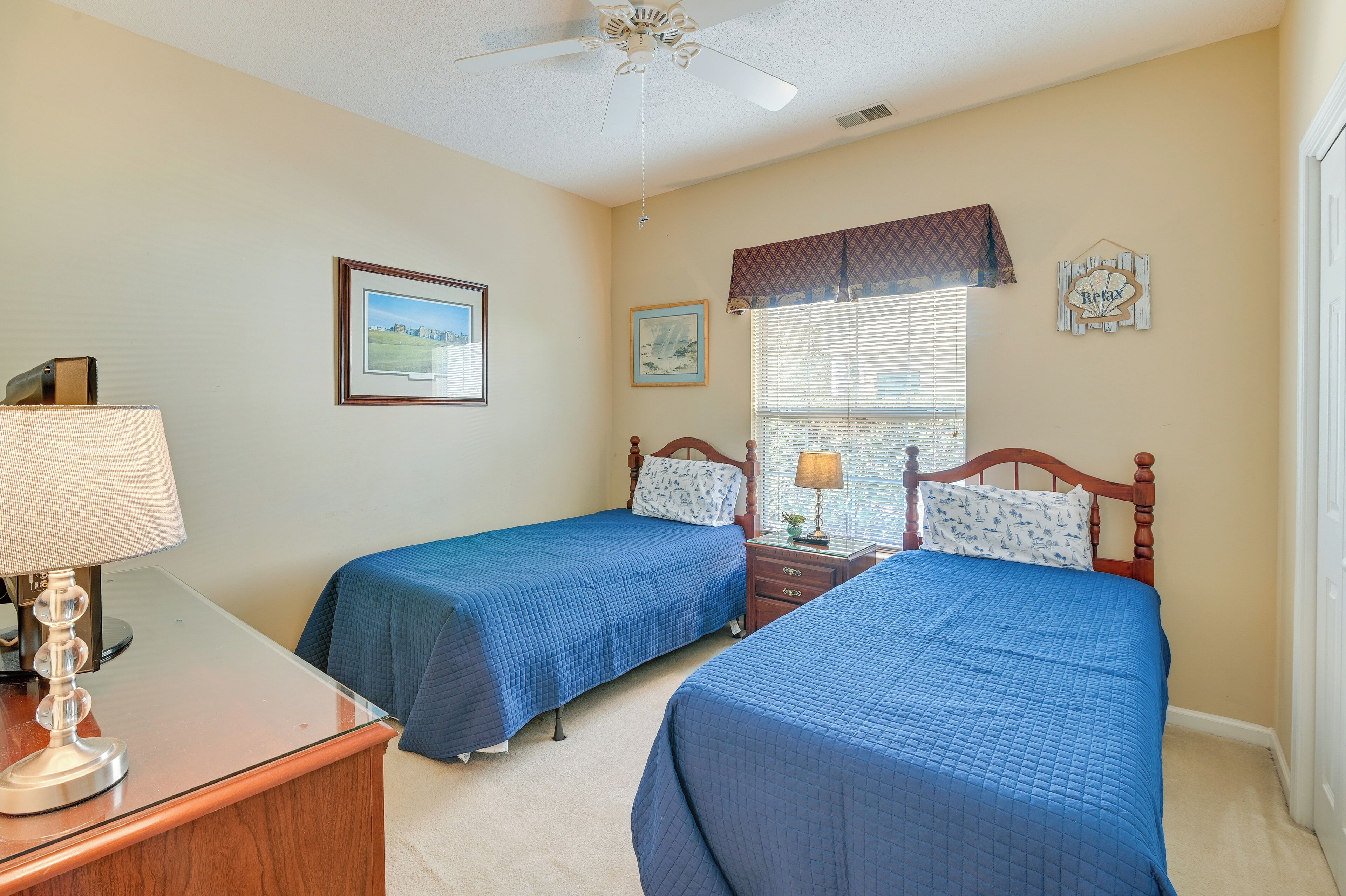 A bedroom with two beds, a desk, a lamp, and a ceiling fan.