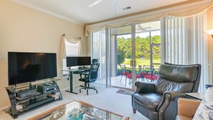 A living room with a flat-screen TV, a glass coffee table, a leather sofa, and a sliding glass door leading to a patio with outdoor furniture. - Myrtle Beach Condo w/ Community Perks (Myrtle Beach)