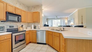 A kitchen with wooden cabinets, stainless steel appliances, a dishwasher, and a large window. - Myrtle Beach Condo w/ Community Perks (Myrtle Beach)