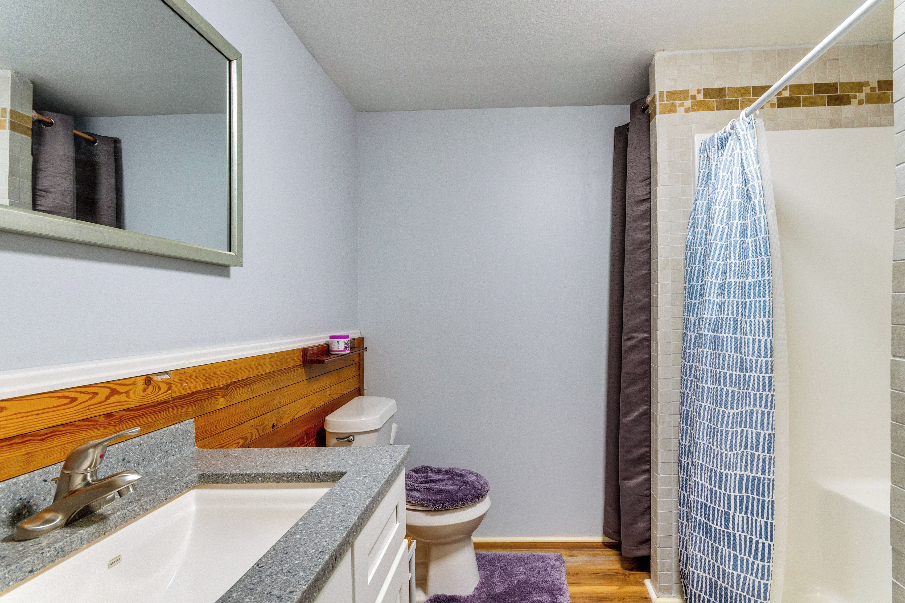 A bathroom with a wooden vanity, a white sink, a toilet, and a shower with a blue shower curtain.