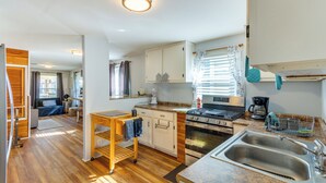 Una cocina compacta con suelo de madera, armarios blancos, estufa y lavamanos.
