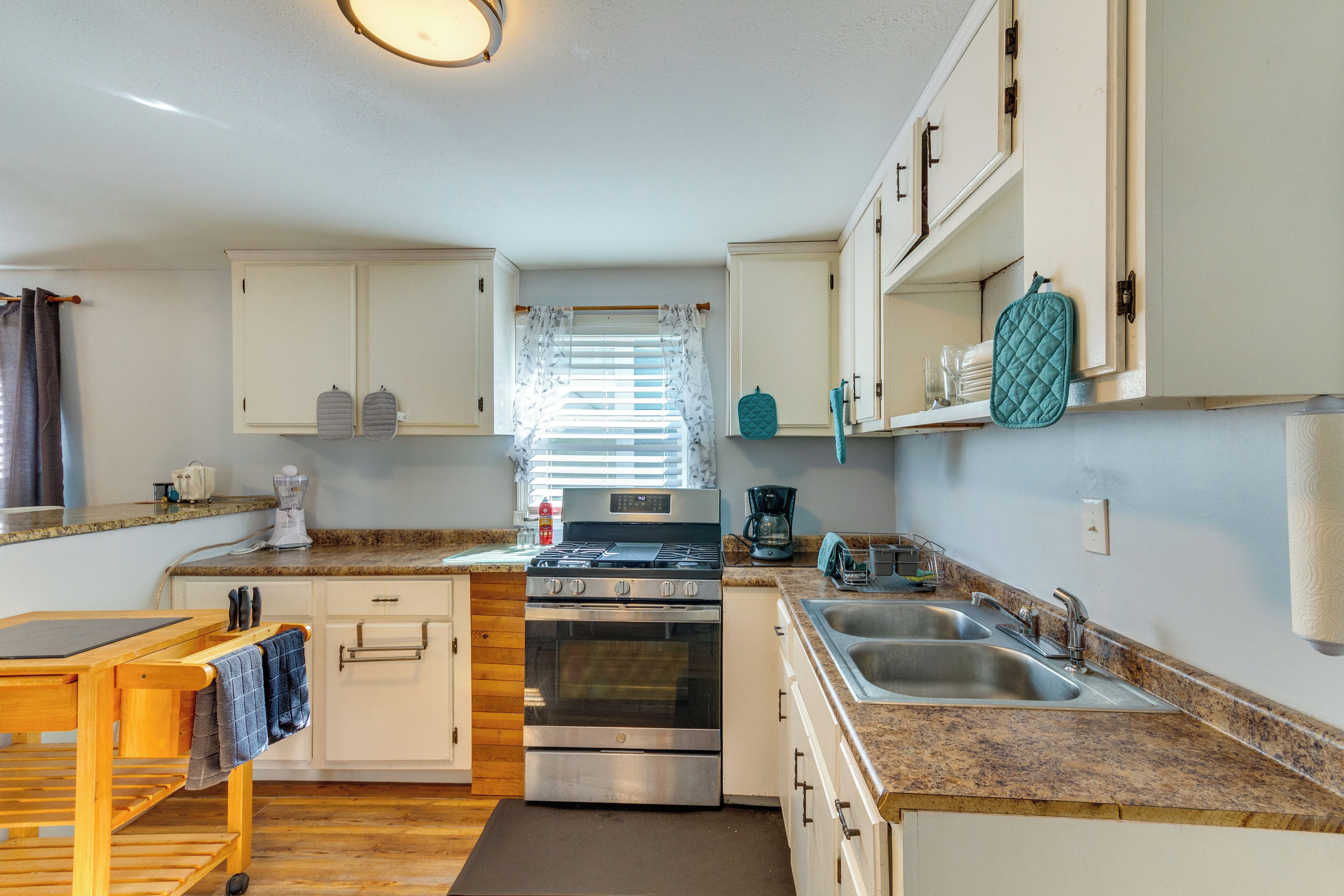 A compact kitchen with white cabinets, a stainless steel stove, a sink, and a wooden countertop.