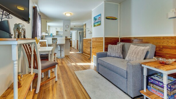 Una sala acogedora con un sofá gris, suelo de madera y una zona de comedor con mobiliario blanco.