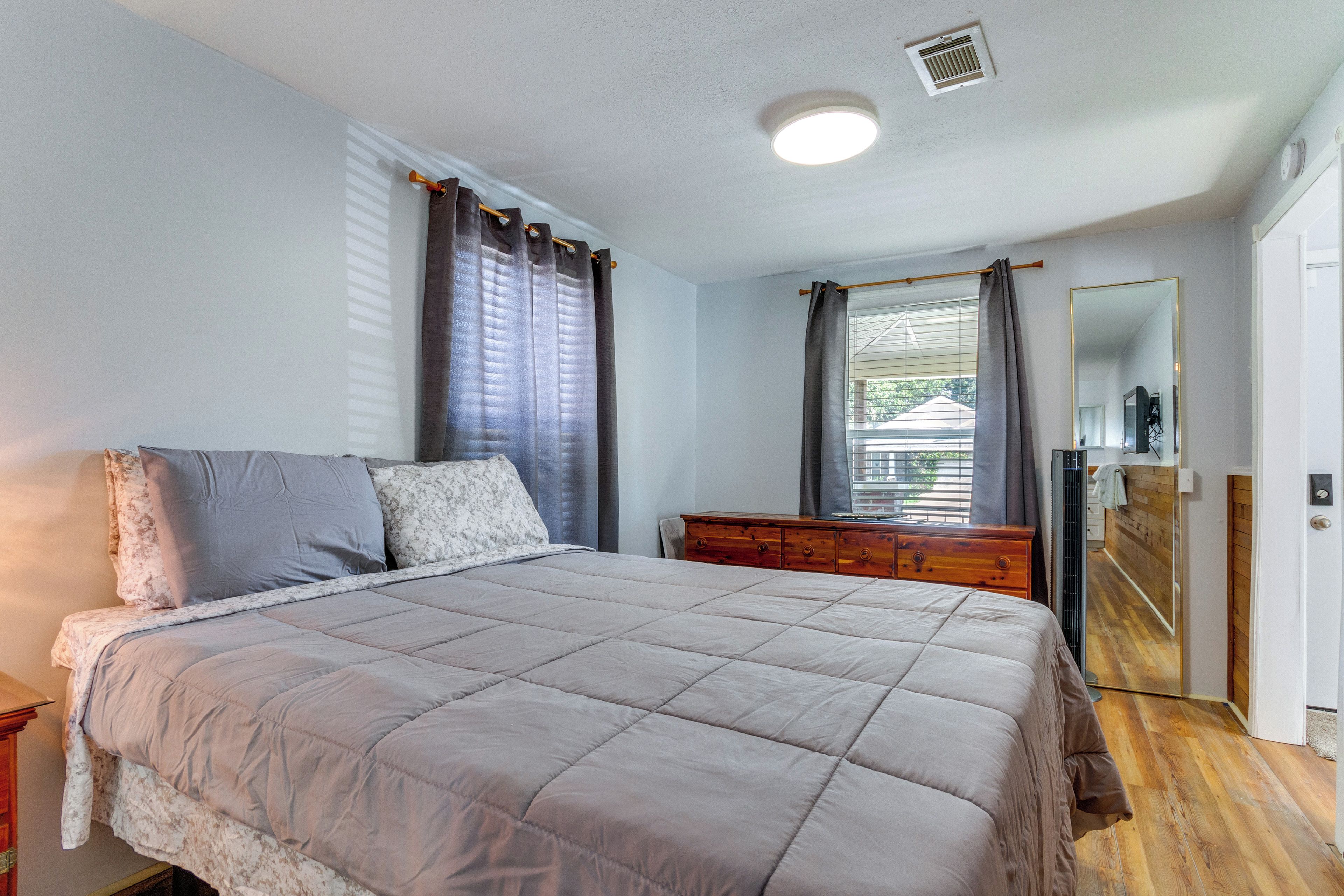 A bedroom with a large bed, a dresser, a mirror, and a window with curtains.