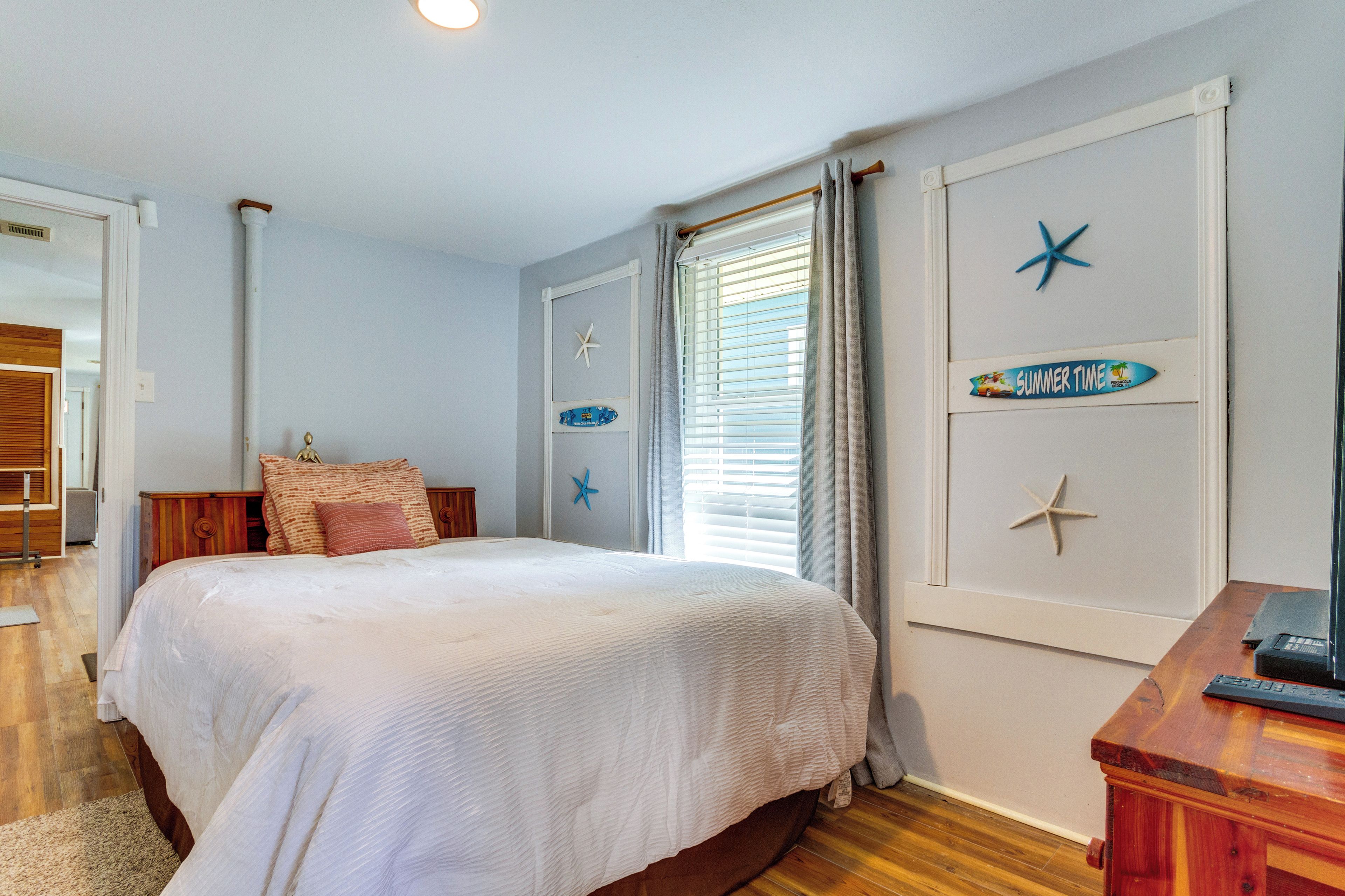A bedroom with a large bed, wooden headboard, and a nightstand. There are starfish decorations on the wall and a sign that says "SUMMER TIME".