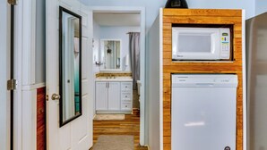 Una cocina compacta con microondas y lavavajillas integrados en un mueble de madera, una puerta blanca y suelo de madera.