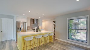 A modern kitchen with a yellow island, white bar stools, and a stainless steel refrigerator. - Peaceful Hot Springs Home: Deck w/ Water Views! (Hot Springs)