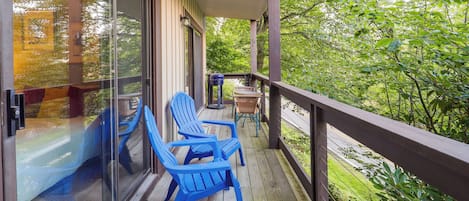 A wooden deck with blue Adirondack chairs and a table, overlooking a lush green landscape.