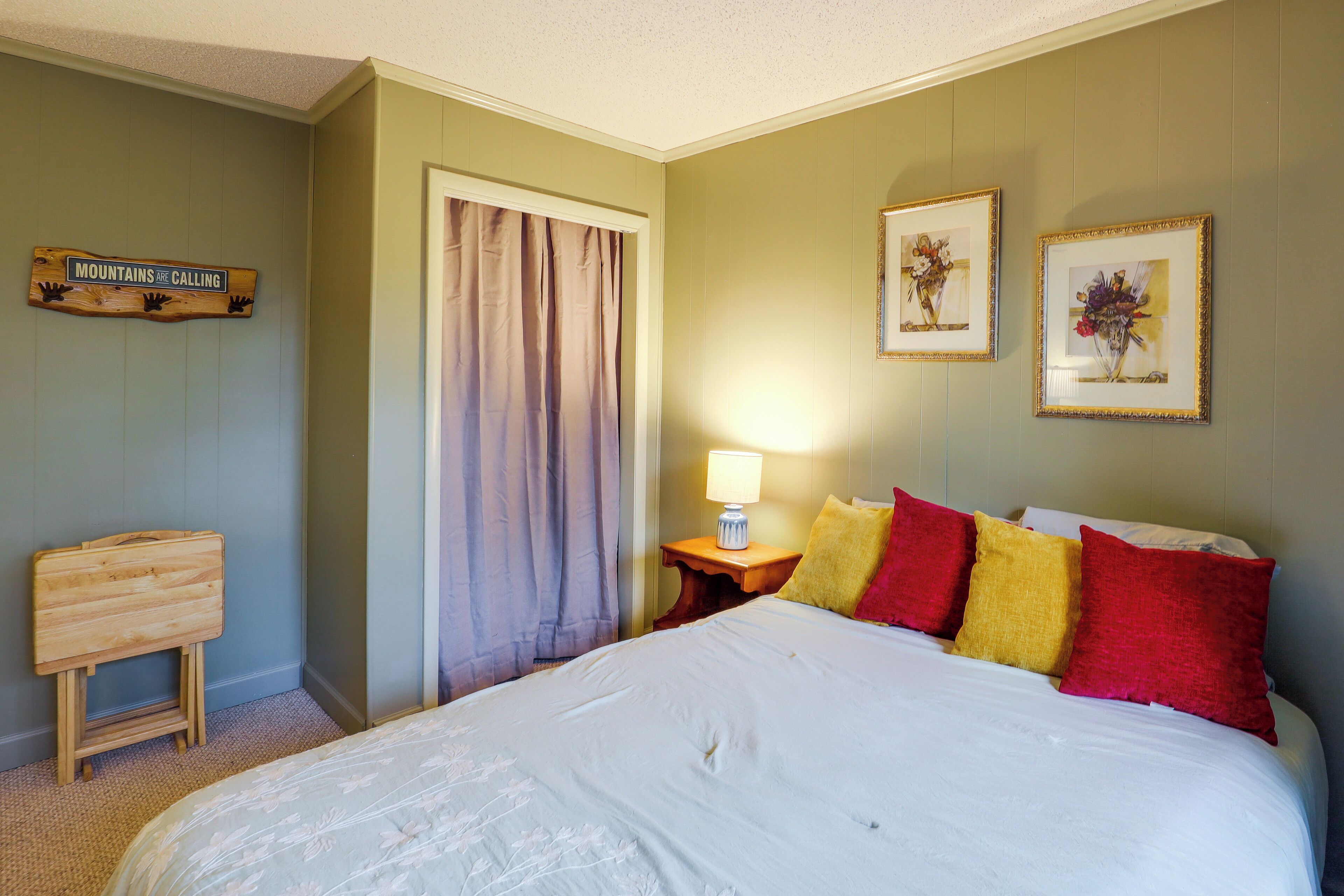 A bedroom with a bed, a nightstand with a lamp, a wooden headboard, a door with curtains, and two framed pictures on the wall.