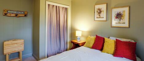 A bedroom with a bed, a nightstand with a lamp, a wooden headboard, a door with curtains, and two framed pictures on the wall.
