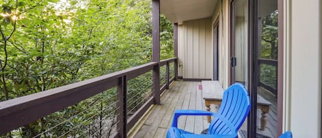 A wooden deck with a railing, two blue chairs, and a table.