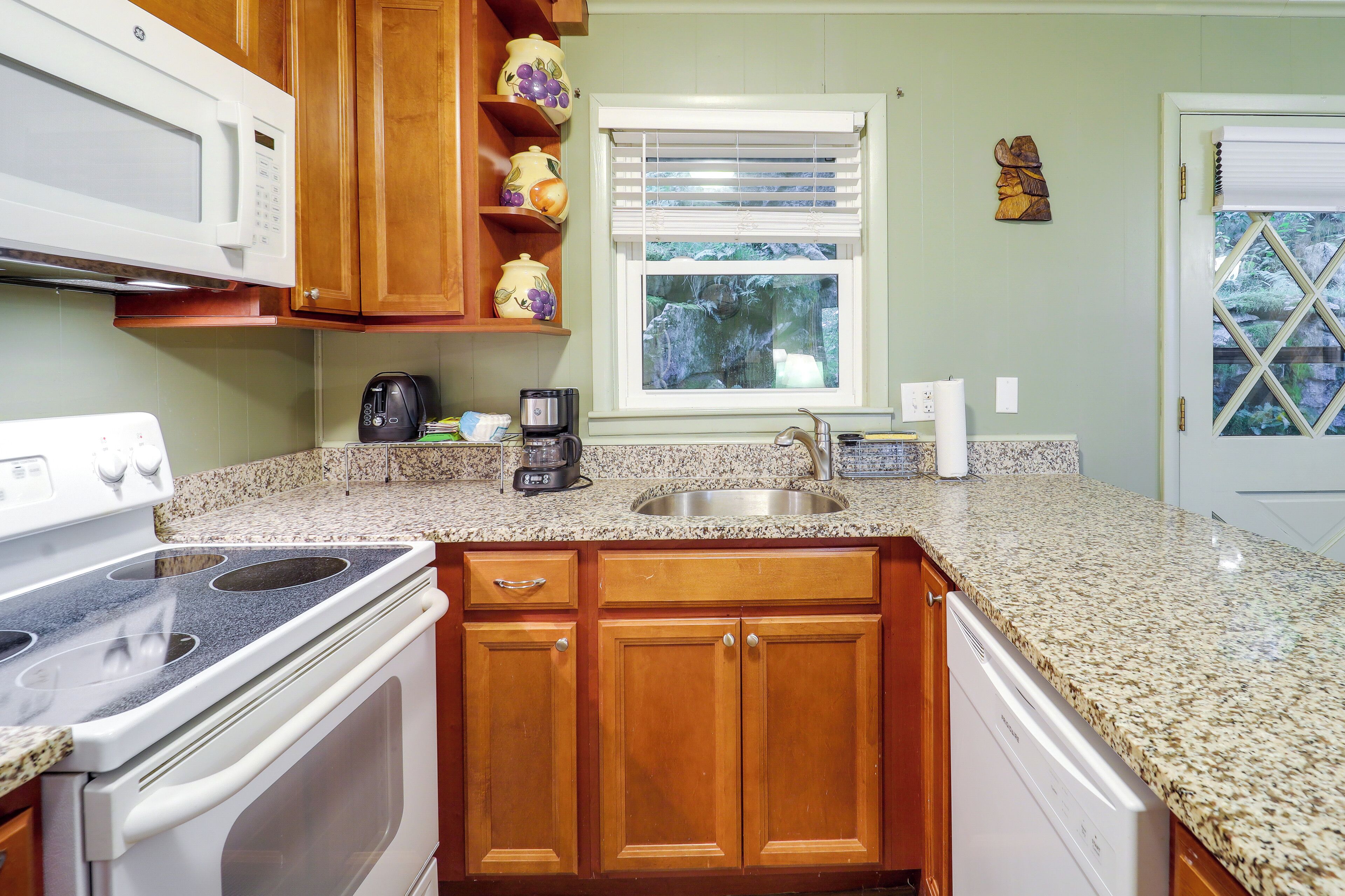 A kitchen with wooden cabinets, a granite countertop, a stainless steel sink, a microwave, a stove, and a window with blinds.